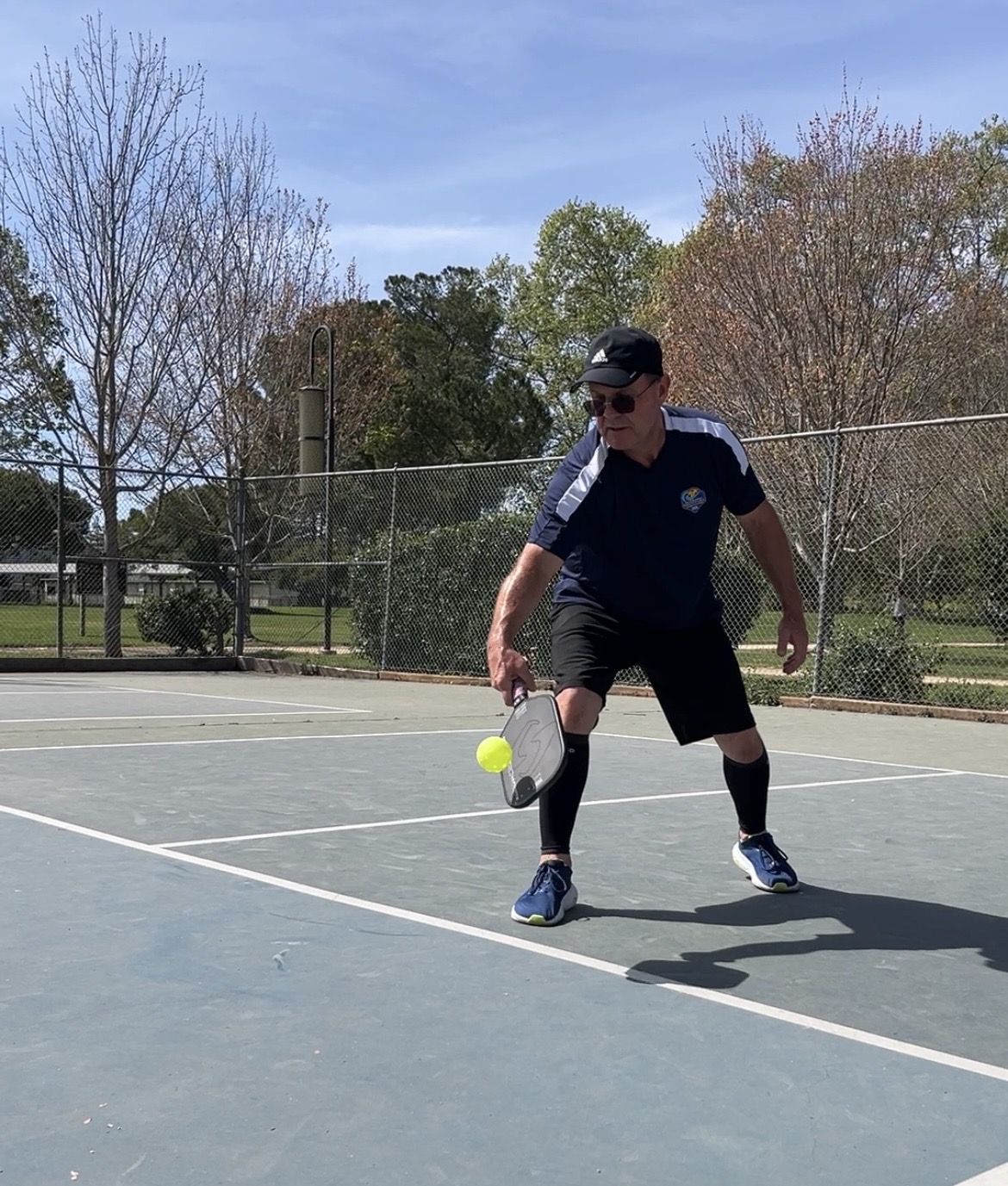 Older pickleball player reaching low for a ball on court