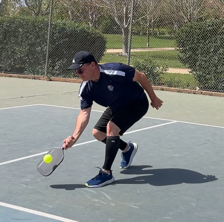 Pickleball player reaching low for a ball on court.